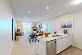 Located on Duke Street East in Kitchener, Ontario, this well-appointed 2-bedroom, 2-bathroom unit offers a thoughtfully designed, single-floor layout. The welcoming entryway, finished with light wood flooring, opens into a bright and airy hallway that leads to the main living area. The open-concept kitchen and living room form the heart of the space, featuring a sleek white kitchen island with a double sink, stainless steel appliances including a dishwasher, range, microwave, and refrigerator, and ample white cabinetry. The island doubles as a breakfast bar with seating, flowing seamlessly into the combined dining and living area, which is bathed in natural light from large sliding windows that offer views of the surrounding cityscape. Plush carpeting throughout the living and bedroom areas adds warmth and comfort. The primary bedroom is generously sized, boasting a large window with expansive outdoor views and access to a walk-in closet with built-in wire shelving. Both bathrooms are clean and functional, with one featuring a tub-shower combination and wood-look vinyl flooring. A dedicated in-suite laundry room houses a stacked washer and dryer unit alongside additional shelving. Recessed lighting throughout enhances the modern, bright ambiance of this well-designed Kitchener residence.