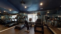Located at 100 Eclipse Dr in Cary, NC, this fitness center is a well-equipped, single-floor facility designed to support a full range of workout routines. The space is divided into two distinct areas, each thoughtfully outfitted for different training needs.

The main cardio and machine room features a striking vaulted ceiling painted in a deep navy blue, creating a sleek, modern atmosphere. Recessed lighting and ceiling fans keep the space well-lit and ventilated. Full-length wall mirrors visually expand the room and allow users to monitor their form while training. This area houses a comprehensive selection of TRUE-brand cardio equipment, including treadmills, ellipticals, a stair climber, and a recumbent bike, as well as a cable machine and weight bench. Natural light filters in through multiple windows fitted with blinds.

The second area is a dedicated strength training room with a darker, bold aesthetic — deep charcoal walls and black ceilings paired with recessed lighting. This space features a Smith machine, weight benches, free weights, and additional cable and functional training equipment. Durable hard flooring provides a stable surface for lifting.

Together, the two zones offer a comprehensive fitness experience suitable for both cardio conditioning and strength training.