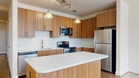 Located at 2677 Avenir Pl in Vienna, VA, this well-appointed two-bedroom, two-bathroom residence offers a thoughtfully designed single-floor layout. The modern kitchen is a standout feature, showcasing warm wood cabinetry, crisp white quartz countertops, a central island, stainless steel appliances including a refrigerator, range, microwave, and dishwasher, and pendant lighting that adds a refined touch. The kitchen flows naturally into the combined dining and living area, which features light hardwood flooring and access to a private balcony. The bedrooms are carpeted and filled with natural light from large windows, offering views of the surrounding neighborhood. The generously sized primary bedroom includes direct access to a walk-in closet equipped with wire shelving systems for ample storage. Two additional closets serve the rest of the home. The bathrooms are finished with tile flooring, and one features a glass-enclosed walk-in shower. A dedicated laundry space adds everyday convenience. A bright hallway with hardwood floors and flush ceiling lighting connects the living and sleeping areas seamlessly. Throughout the home, neutral tones, clean lines, and quality finishes create a cohesive and welcoming atmosphere.