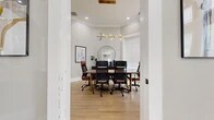 Located at 300 Bardin Greene Dr in Arlington, TX, this single-floor commercial space offers a thoughtfully designed interior that blends modern elegance with functional sophistication. Light hardwood flooring flows seamlessly throughout, complementing the neutral gray walls and crisp white trim that define the aesthetic.

The main lounge area is a standout feature, boasting soaring ceilings with a striking octagonal coffered detail and an abundance of natural light pouring in through oversized windows dressed in clean white blinds. Plush navy blue accent chairs are arranged atop geometric-patterned area rugs, while glass-panel folding doors with brass hardware create a dramatic and flexible division between spaces. A separate seating zone near the entrance features additional blue barrel chairs set against floor-to-ceiling windows, giving the area an open, airy feel.

The conference room is equally impressive, centered around a warm walnut conference table surrounded by ergonomic leather-and-mesh chairs. A sculptural brass chandelier adds a refined touch overhead, while bold navy abstract wall art, a circular mirror, and a decorative sideboard contribute to the room's polished character. Multiple windows ensure the space remains bright and inviting throughout the day.

Together, these areas create a cohesive, professionally curated environment ideal for client-facing operations or collaborative work.