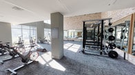 Located at 11108 W Chandler Blvd in Los Angeles, CA, this single-floor fitness center offers a well-appointed and spacious workout environment designed to support a full range of exercise activities. The facility is defined by its striking architectural character, including soaring ceilings with exposed structural beams, warm exposed brick accent walls, and an abundance of natural light streaming through floor-to-ceiling windows that frame views of the surrounding area.

The strength training zone features multiple Matrix power rack systems arranged to accommodate simultaneous use, complemented by large wall-mounted mirrors that enhance the sense of space and allow users to monitor their form. Rubber-backed carpeted flooring throughout provides comfort and durability underfoot.

The cardio area is equally well-equipped, housing a selection of spin bikes, air bikes, and rowing machines positioned to take full advantage of the natural light from the expansive glazed facade. A dedicated accessories station displays stability balls, medicine balls, resistance bands, and foam rollers, supporting flexibility and functional training needs.

Structural columns punctuate the open floor plan, adding to the industrial-modern aesthetic while defining distinct zones within the facility. The overall ambiance is bright, clean, and energizing, making this fitness center a compelling and fully equipped destination for exercise.