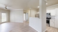 This single-story, 3-bedroom, 2-bathroom home offers a well-designed open-concept layout finished with light-toned luxury vinyl plank flooring throughout. The living area features notable vaulted ceilings with crown molding and a ceiling fan, creating an airy, spacious feel, while a large window fills the room with natural light. Decorative columns define the transition between the living space and the kitchen, which is outfitted with white cabinetry, granite-style countertops, a breakfast bar peninsula, and a full suite of stainless steel appliances including a refrigerator, electric range, and over-the-range microwave. Three well-proportioned bedrooms are connected via a series of hallways, offering a practical layout with two closets for storage. The primary bedroom provides a comfortable retreat with its own dedicated space. Both bathrooms are finished in neutral tones, with one featuring a full soaking tub with tiled surround. A dedicated in-unit laundry room accommodates a full-size washer and dryer. The attached garage provides convenient enclosed parking and additional storage. Throughout, warm beige walls and consistent flooring create a cohesive, neutral aesthetic ideal for a variety of living arrangements.