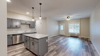 Located at 2988 Radio Rd in River Falls, Wisconsin, this well-appointed single-story home offers three bedrooms and two bathrooms across a thoughtfully designed floor plan. The open-concept kitchen and living area serves as the heart of the home, featuring gray shaker-style cabinetry with matte black hardware, a granite-topped center island with pendant lighting overhead, stainless steel appliances, and durable wood-look luxury vinyl plank flooring. The living room extends naturally from the kitchen, brightened by a large window and a ceiling fan, creating a welcoming, airy atmosphere. A glass-paneled entry door adds additional natural light to the space. The bedrooms are carpeted for comfort, with the generously sized primary bedroom offering a ceiling fan and direct access to a walk-in closet equipped with wire shelving systems. Secondary bedrooms feature narrow horizontal windows that allow natural light while maintaining privacy. The two bathrooms are finished with matching gray cabinetry, dual-sink vanities, large mirrors, and wood-look flooring, maintaining a cohesive aesthetic throughout. Two dedicated closets provide ample storage. The neutral color palette and modern finishes give the entire home a clean, move-in-ready appeal.