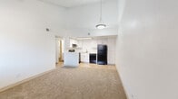 Located at 2120 N Silverbell Rd in Tucson, Arizona, this one-bedroom, two-bathroom residence offers a thoughtfully arranged single-floor layout designed to maximize functionality within a cozy footprint. The open-concept living and kitchen area is a standout feature, highlighted by soaring vaulted ceilings that lend an airy, spacious feel well beyond the unit's physical dimensions. A pendant light fixture anchors the living area, while a skylight above the kitchen fills the space with natural light. The kitchen is well-appointed with crisp white cabinetry, a black electric range, dishwasher, refrigerator, and a peninsula that subtly separates the cooking space from the carpeted living area. Tile-style flooring runs throughout the kitchen for easy maintenance. The bedroom is a comfortable, quiet retreat featuring plush carpet, a window with blinds for natural light and privacy, and direct access to a dedicated closet. Both bathrooms are finished cleanly in white, with shaker-style vanity cabinetry, speckled countertops, framed mirrors, and wood-look flooring. One bathroom includes a full tub-shower combination. The unit's neutral white walls and consistent finishes throughout create a clean, move-in-ready ambiance.
