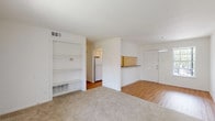 This single-floor residence offers a thoughtfully organized layout with a clean, neutral aesthetic throughout. The open living area is finished with plush wall-to-wall carpeting and transitions seamlessly into a hardwood-style floored dining and entry zone, creating a natural distinction between spaces. A set of built-in shelving units lines one wall of the living area, providing practical storage and display options alongside a floor-level vent for climate control. A pass-through counter connects the living space to the kitchen, which features speckled stone-look countertops, white cabinetry, hardwood-style flooring, and access to a dedicated pantry closet with built-in shelving. The bedrooms are carpeted and bright, each equipped with ceiling fans and windows fitted with vertical blinds that allow for natural light control. At least one bedroom includes access to a generously sized walk-in closet with wrap-around hanging rods. The bathrooms maintain a crisp, clean look with white square tile surrounding full-size soaking tubs and shower combinations, complemented by hardwood-style flooring. The front entry door opens into the main living space, where a pendant light fixture adds a subtle decorative touch to the overall bright and functional interior.