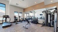 Located in Colorado Springs, CO, this modern fitness center offers a comprehensive exercise space designed to support a wide range of workout routines. The room features a clean, contemporary aesthetic with crisp white walls accented by warm tan upper panels, recessed lighting, and neutral-toned carpet flooring throughout.

Large windows line multiple walls, flooding the space with abundant natural light and providing views of the surrounding outdoor area, including glimpses of a pool and the Colorado landscape. A full-length mirror along one wall visually expands the room and enhances the open, airy feel.

The facility is outfitted with an impressive array of equipment, including multiple treadmills, upright and recumbent stationary bikes, a rowing machine, and a cable/multi-functional strength machine. A dumbbell rack stocked with a full range of free weights and an adjustable weight bench provide options for strength training. Medicine balls and resistance accessories are also available for functional fitness workouts, and a mounted flat-screen display offers additional utility.

Glass-panel doors connect to an adjacent room, contributing to the open, community-oriented layout. The overall ambiance is bright, clean, and functional, making this fitness center a well-appointed space for residents seeking convenient, on-site exercise facilities.