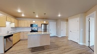 This single-floor unit is designed with a practical, open layout that connects the kitchen and living areas seamlessly. The kitchen serves as the centerpiece, featuring light maple cabinetry, granite-topped counters, and a full suite of stainless steel appliances including a gas range, built-in microwave, dishwasher, and refrigerator. A center island with a matching granite surface provides additional workspace and is illuminated by dual pendant lights overhead, while recessed lighting brightens the broader kitchen area. Light wood-style vinyl plank flooring runs throughout the main living spaces, contributing to a clean, cohesive aesthetic.

The open living area extends generously from the kitchen, offering ample room for comfortable furnishings. A ceiling fan provides air circulation, and a baseboard heating system ensures year-round comfort. A window in the bedroom allows natural light to fill the carpeted space, which also features its own ceiling fan. Two bathrooms serve the unit; one includes a tub-shower combination with a vanity and light maple cabinetry, while the other offers a single vanity and shower area. An attached two-car garage with an automatic opener provides substantial enclosed parking and additional storage space.