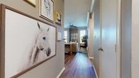 Located in Benbrook, TX, this single-story 2-bedroom, 2-bathroom home offers a practical and stylish layout across a comfortable footprint. The entryway hallway makes a strong first impression, lined with wall art and rich wood-look flooring that flows throughout the main living areas. The living room features crown molding, a ceiling fan, and natural light from multiple windows with blinds, creating a bright and inviting atmosphere. Adjacent to the living area, the dining space benefits from large windows that flood the room with natural light, complementing the warm hardwood-style floors. The kitchen is equipped with warm-toned wood cabinetry, granite-style countertops, a breakfast bar peninsula, and black appliances including a full-size refrigerator and built-in microwave. The primary bedroom offers a carpeted retreat with a walk-in closet featuring built-in wire shelving and a window for natural light. The second bedroom also features plush carpeting and a bright window. Both bathrooms include a tub-shower combination with clean white tile accents and a contrasting dark tile border detail. Throughout the home, neutral gray-toned walls, wood-look and carpet flooring, and ample closet storage provide a functional and cohesive living environment.