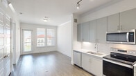 This thoughtfully designed single-floor residence combines contemporary style with functional living. The open-concept layout seamlessly connects the kitchen and living area, creating a bright and airy atmosphere enhanced by light wood-style flooring that runs throughout the space.

The kitchen is a standout feature, outfitted with sleek grey high-gloss cabinetry, white quartz countertops, and a marble-style tile backsplash. A full suite of stainless steel appliances — including a refrigerator, electric range, built-in microwave, and dishwasher — is complemented by track lighting overhead and a deep undermount sink. Ample upper and lower cabinet storage adds practicality to the polished aesthetic.

The living area is filled with natural light, thanks to large windows fitted with horizontal blinds and a glass-paneled exterior door that opens to a balcony with views of the surrounding neighborhood. Crown molding accents the ceilings throughout, lending a refined touch to each room.

The bedrooms are generously sized, each featuring large windows that draw in natural light and offer pleasant outdoor views. Clean white walls and consistent flooring create a calm, neutral environment. A bathroom and additional closet space complete the layout, making this a well-rounded, move-in-ready residence with a clean modern finish.
