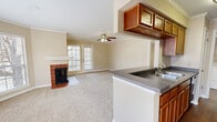 This well-appointed 2-bedroom, 3-bathroom single-floor residence offers a functional and comfortable layout across a thoughtfully designed floor plan. The open-concept kitchen and living area serves as the heart of the home, where a peninsula with dark granite-style countertops and warm wood cabinetry connects the kitchen to the carpeted living room. The living space is highlighted by a brick wood-burning fireplace, crown molding, a ceiling fan, and a glass door leading to a private balcony that allows natural light to fill the room. A bay window area further enhances the brightness of the living space. The kitchen features hardwood-style flooring, ample cabinetry, a double-basin sink, and a full suite of appliances including a refrigerator. A dedicated laundry room with stacked units is conveniently accessible from the kitchen hallway. Both bedrooms are carpeted and finished with crown molding and ceiling fans. The primary bedroom includes a walk-in closet and a window with outdoor views. The bathrooms are clean and functional, each featuring tub-shower combinations with white tile surrounds. With five closets throughout, storage is plentiful, completing this practical and inviting residence.