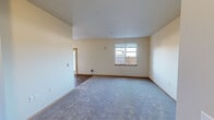 This single-floor unit in Yelm, WA presents a practical and cohesive layout designed for comfortable everyday living. The living area is generously proportioned, featuring neutral-toned walls, plush carpeting, and a window fitted with blinds that allows natural light to filter in while offering outdoor views. A transition to wood-look flooring marks the entry zone adjacent to the living space.

The kitchen is well-equipped, showcasing dark espresso cabinetry with sleek bar-pull hardware, granite-style countertops, and black appliances including a full-size refrigerator, dishwasher, and microwave. The adjoining dining area features wood-look flooring, a pendant light fixture, and a glass-paneled door alongside additional windows that brighten the space considerably.

The bedrooms are carpeted and finished with the same warm neutral palette. Each includes a sliding-door closet with a hanging rod, providing organized storage. The bathroom features a double-sink vanity with dark cabinetry, a full bathtub with a shower, tile flooring, and a lighted mirror above — offering a functional and tidy finish throughout.