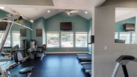 Located at 5 Marcia Way in Roseville, CA, this fitness center is a thoughtfully designed, single-floor facility that provides residents with a comprehensive workout environment. The space features vaulted ceilings that lend an open, airy feel, complemented by a ceiling fan and recessed lighting throughout. Teal accent walls paired with crisp white trim create a clean, energizing aesthetic that carries through the entire facility.

The main workout area is anchored by a row of treadmills positioned in front of large windows that frame views of the outdoor pool area, allowing natural light to flood the space and providing a pleasant backdrop during cardio sessions. A wall-mounted flat-screen television enhances the experience for those using the cardio equipment. Durable dark rubber flooring covers the entire space, providing safety and support during exercise.

A dedicated strength training area houses a variety of resistance machines, including Matrix and Hoist brand equipment, along with a multi-station cable machine and stationary bikes. Full-length wall mirrors in the strength zone visually expand the space and allow users to monitor their form. Additional windows in this section bring in supplementary natural light. The fitness center also displays posted room rules, reflecting an organized and community-minded facility.