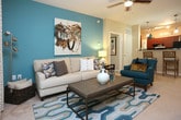 This single-floor residence offers a thoughtfully designed layout with a cohesive, contemporary aesthetic throughout. The galley-style kitchen is well-equipped with rich dark wood cabinetry, dark granite countertops, black appliances including a gas range and refrigerator, a double sink, and warm hardwood flooring. Track and pendant lighting illuminate the space effectively, and a pass-through connects the kitchen to the rest of the living areas. The dining area features an eye-catching textured accent wall paired with a glass-top table, creating an intimate yet stylish setting. The living room is bright and welcoming, anchored by a bold teal accent wall, plush carpeting, a ceiling fan, and French doors that open to an outdoor patio, allowing abundant natural light. The primary bedroom offers a serene retreat with a teal accent wall, large windows with outdoor views, and an en-suite bathroom. Additional bedrooms are well-sized with ample natural light, carpeted floors, and generous window treatments. The bathrooms are clean and functional, featuring tiled tub-shower combinations and vanities with ample storage. Throughout the residence, a consistent palette of warm neutrals and teal accents creates a unified and inviting ambiance.