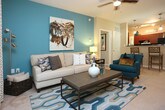 This single-floor residence offers a thoughtfully designed layout with a cohesive, contemporary aesthetic throughout. The galley-style kitchen is well-equipped with rich dark wood cabinetry, dark granite countertops, black appliances including a gas range and refrigerator, a double sink, and warm hardwood flooring. Track and pendant lighting illuminate the space effectively, and a pass-through connects the kitchen to the rest of the living areas. The dining area features an eye-catching textured accent wall paired with a glass-top table, creating an intimate yet stylish setting. The living room is bright and welcoming, anchored by a bold teal accent wall, plush carpeting, a ceiling fan, and French doors that open to an outdoor patio, allowing abundant natural light. The primary bedroom offers a serene retreat with a teal accent wall, large windows with outdoor views, and an en-suite bathroom. Additional bedrooms are well-sized with ample natural light, carpeted floors, and generous window treatments. The bathrooms are clean and functional, featuring tiled tub-shower combinations and vanities with ample storage. Throughout the residence, a consistent palette of warm neutrals and teal accents creates a unified and inviting ambiance.
