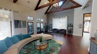 Located at 8401 Medlock Dr in Fort Worth, Texas, this single-story clubhouse is defined by its dramatic architectural character and welcoming interior design. The centerpiece of the space is a soaring vaulted ceiling supported by bold, exposed dark wood trusses and finished with white shiplap paneling, creating a striking contrast that draws the eye upward. A chandelier suspended from the peak adds an elegant focal point to the open main lounge area.

Rich, dark hardwood flooring runs throughout, grounding the space with warmth and continuity. The main lounge is generously proportioned, furnished with a curved sectional sofa and a botanical-patterned area rug surrounding a glass-top coffee table. A pair of charcoal armchairs provides additional seating near large windows dressed with sheer white curtains that invite abundant natural light.

A natural stone fireplace serves as a standout feature in an intimate seating alcove, complemented by a wall-mounted mirror and a bistro-height table with bar-style chairs. Adjacent to the lounge, a coffee and refreshment station is set against a textured stone accent wall with slate-blue cabinetry, granite counters, and a wall-mounted television above.

French doors lead directly to a fitness center visible from the main lounge, offering convenient access to exercise equipment. The overall ambiance is modern yet rustic, cohesive and inviting throughout.