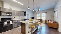 This thoughtfully designed single-floor residence offers a smart, efficient layout across seven distinct rooms, including a bedroom, two bathrooms, a kitchen, living room, office, and laundry space. The open-concept kitchen and living area serves as the heart of the home, showcasing grey shaker-style cabinetry, granite countertops, stainless steel appliances, and a central island with seating for casual dining — all illuminated by a row of stylish pendant lights. Wood-style flooring flows throughout, tying the spaces together seamlessly. The living room is bright and welcoming, featuring multiple large windows that flood the space with natural light and offer views of the surrounding neighborhood. The bedroom is a calm, comfortable retreat with hardwood-style floors, neutral tones, and access to a well-organized walk-in closet. Both bathrooms are finished with granite-topped vanities and grey cabinetry consistent with the kitchen's design. A dedicated office provides a functional workspace, while the in-unit laundry room adds everyday convenience. The overall ambiance is modern and cohesive, with clean lines, warm tones, and quality finishes throughout that make efficient use of every square foot.