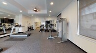 The 745 Hamilton St Fitness Center in Somerset, NJ is a thoughtfully designed, single-floor facility offering a comprehensive workout environment for a range of fitness needs. The space is divided into distinct functional zones, each tailored to a specific type of training.

The cardio area is equipped with multiple Landice treadmills and elliptical machines, positioned in front of a large floor-to-ceiling mirror wall that reflects natural light from surrounding windows and amplifies the sense of space. A mounted flat-screen TV provides entertainment during workouts.

Adjacent to the cardio zone is a strength training area featuring a multi-functional cable machine, an adjustable weight bench, and a tiered dumbbell rack stocked with a full range of free weights. Durable rubber flooring throughout this section ensures safety and stability during lifts.

A dedicated cycling studio houses several stationary spin bikes alongside exercise balls and a fitness accessory station, all set on smooth hardwood-style flooring that lends a clean, open feel to the room.

Perhaps the standout feature is a spacious studio area lined with expansive floor-to-ceiling mirrors and equipped with a large display screen for guided workouts or virtual classes. Recessed lighting and a tray ceiling with a decorative light fixture add a polished, upscale touch to the overall environment.