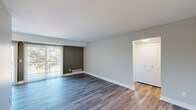 This 1-bedroom, 1-bathroom unit offers a thoughtfully designed layout across a single floor, making efficient use of its space. The open-concept living and kitchen area serves as the heart of the unit, with the living room featuring durable hardwood-style flooring, neutral gray wall tones, and a large sliding glass door fitted with vertical blinds that invites natural light and provides views of the surrounding greenery. A dark accent wall adds a subtle design touch to the living space, which also includes a closet and entryway near the front door.

The galley-style kitchen is a standout feature, boasting white shaker cabinetry with brushed gold hardware, a gray subway tile backsplash, light countertops, a stainless steel sink, and a full suite of stainless steel appliances including a refrigerator, range, microwave, and dishwasher. Recessed and flush-mount lighting completes the space.

The bedroom is a comfortable size, featuring a window with vertical blinds that frames a wooded outdoor view, continued hardwood-style flooring, and access to a dedicated closet. The full bathroom includes a tub/shower combo, a white vanity with a clean countertop, and matching hardwood-style flooring, offering a bright and functional finish.