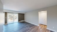 This 1-bedroom, 1-bathroom unit offers a thoughtfully designed layout across a single floor, making efficient use of its space. The open-concept living and kitchen area serves as the heart of the unit, with the living room featuring durable hardwood-style flooring, neutral gray wall tones, and a large sliding glass door fitted with vertical blinds that invites natural light and provides views of the surrounding greenery. A dark accent wall adds a subtle design touch to the living space, which also includes a closet and entryway near the front door.

The galley-style kitchen is a standout feature, boasting white shaker cabinetry with brushed gold hardware, a gray subway tile backsplash, light countertops, a stainless steel sink, and a full suite of stainless steel appliances including a refrigerator, range, microwave, and dishwasher. Recessed and flush-mount lighting completes the space.

The bedroom is a comfortable size, featuring a window with vertical blinds that frames a wooded outdoor view, continued hardwood-style flooring, and access to a dedicated closet. The full bathroom includes a tub/shower combo, a white vanity with a clean countertop, and matching hardwood-style flooring, offering a bright and functional finish.