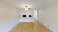 Located at Cedar Hills Blvd in Minnetonka, Minnesota, this one-bedroom, one-bathroom unit offers a well-organized single-floor layout. The open-concept living and kitchen area is anchored by light wood-style flooring and a pendant light fixture, creating a bright and welcoming atmosphere. The kitchen features a pass-through peninsula with a breakfast bar, white cabinetry with modern hardware, light countertops, and black stainless appliances including an electric range with microwave and a dishwasher. A closet provides additional storage just off the kitchen.

The spacious primary bedroom is finished with plush carpet, a baseboard heating system, and a window that invites natural light and outdoor views of the surrounding neighborhood. An additional room with wood-style flooring and baseboard heating offers flexible use as a dining area or home office.

The bathroom is finished with wood-style flooring, a white vanity with granite-style countertops, Hollywood-style vanity lighting, and accessibility-friendly grab bars near the toilet and shower area. Neutral, warm beige tones throughout the unit create a cohesive and calm aesthetic. Sliding glass door access to the exterior is also visible, adding to the unit's connectivity with the outdoors.
