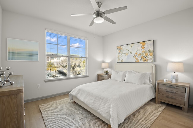 Bright and airy bedroom featuring a cozy bed, stylish artwork, natural wood furnishings, and large windows with a refreshing view. - Avana Parkway