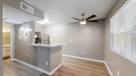 This single-floor residence offers a clean, modern aesthetic defined by neutral warm-gray walls, white trim, and wood-look luxury vinyl plank flooring that flows consistently throughout the main living areas. The open-concept layout connects the kitchen and living room seamlessly, creating a functional and inviting shared space. A ceiling fan with a brushed nickel finish anchors the living area, while a window allows natural light to filter in alongside the entry door.

The kitchen is equipped with white shaker-style cabinetry, light speckled countertops, and stainless steel appliances, including a full-size refrigerator and an electric range with an overhead exhaust hood. A peninsula counter provides additional prep space and serves as a natural divider between the kitchen and living area.

The bedroom is a comfortable, well-proportioned room featuring the same wood-look flooring, a window with horizontal blinds for natural light and privacy, and a textured ceiling consistent with the rest of the unit.

The full bathroom is neatly appointed with white cabinetry, a single-sink vanity with a speckled countertop, a large mirror, brushed nickel fixtures and towel bars, and a full tub-shower combination with a white surround. The textured ceilings throughout add a classic finishing detail to this move-in-ready space.