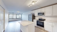 This thoughtfully designed 1-bedroom, 1-bathroom unit spans a comfortable footprint across a single floor, offering a clean, modern aesthetic throughout. The open-concept kitchen and living area serves as the heart of the unit, where a striking marble-look island anchors the kitchen. White shaker-style cabinetry extends to the ceiling, providing ample storage, while stainless steel appliances — including a refrigerator, electric range, built-in microwave, and dishwasher — complete the contemporary kitchen suite. Track lighting illuminates the space with a modern touch.

The living area flows naturally from the kitchen and is bathed in natural light from a large bank of windows fitted with vertical blinds, offering city views. Warm hardwood-style flooring runs consistently throughout the unit, adding cohesion and warmth to each room.

The spacious primary bedroom features its own set of large windows that invite abundant daylight, complemented by a dedicated closet for storage. The full bathroom is tastefully finished with grey tile flooring, a white vanity with quartz countertop, a mirrored medicine cabinet, and a tub-shower combination clad in bold dark stone-look tile. A utility room and hallway complete the layout, ensuring practical functionality throughout.