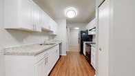 This single-floor residence is thoughtfully laid out to maximize functionality across its key living spaces. The galley-style kitchen serves as a functional centerpiece, featuring crisp white shaker cabinetry with brushed nickel hardware lining both sides of the corridor. Granite-patterned countertops provide ample prep space alongside a stainless steel sink, while black appliances — including a gas range, refrigerator, and dishwasher — add a bold contrast. Warm-toned hardwood-style flooring runs throughout the kitchen, lending a clean, polished aesthetic.

The living area is generously proportioned and finished with neutral-toned carpet, offering a comfortable and versatile space. Large sliding glass doors fitted with vertical blinds draw in natural light and provide outdoor access. The bedrooms are also carpeted and finished in soft gray tones. One bedroom features a walk-in closet with built-in shelving, as well as an attached bathroom entrance, while a second bedroom includes a double-door closet and a window with outdoor views.

The bathroom is finished with white tile flooring and features a full soaking tub with an overhead shower and chrome fixtures. Throughout the unit, a neutral gray palette and clean white trim create a cohesive, understated ambiance.