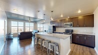 This well-appointed 3-bedroom, 4-bathroom single-floor residence offers a thoughtfully designed open-concept layout with a striking blend of modern and industrial aesthetics. The living area is a standout space, featuring an exposed corrugated metal ceiling, rich hardwood flooring, and a bank of large windows that frame sweeping panoramic views of the surrounding cityscape, flooding the room with abundant natural light.

The kitchen flows seamlessly from the living area and is equipped with stainless steel appliances, dark espresso cabinetry, granite countertops, and a generous island with bar seating beneath stylish pendant lighting — an ideal setup for both everyday living and entertaining.

Each of the three bedrooms is carpeted for comfort, with at least one bedroom offering direct exterior views and built-in under-bed storage. The bedrooms are well-proportioned, with the primary bedroom providing a private, quiet retreat. A dedicated closet adds practical storage to the layout.

The four bathrooms are consistently finished with tile flooring, granite-topped dark wood vanities, and full tub-shower combinations, maintaining a cohesive and clean aesthetic throughout. A hallway connects the private and shared spaces efficiently. Overall, the residence delivers a modern urban living experience with distinctive architectural character and functional design.