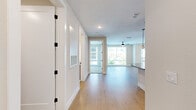 This single-floor residence showcases a contemporary design with a neutral color palette, light hardwood-style flooring, and an abundance of natural light throughout. The entryway opens into a well-connected corridor with black-accented door hardware, providing access to the main living areas.

The kitchen is a standout feature, centered around a generously sized island with a quartz countertop and striking globe pendant lights overhead. Warm wood-toned cabinetry lines the walls, complemented by stainless steel appliances, including a refrigerator with ice maker and a built-in microwave. A dedicated dining or living area adjoins the kitchen, complete with a ceiling fan and large windows that frame outdoor greenery.

The bedrooms are carpeted for comfort and equipped with ceiling fans. Large windows invite natural light and outdoor views, including tropical foliage. One bedroom connects directly to the primary bathroom, which features a soaking tub, a dual-sink vanity with wood cabinetry and matte black fixtures, large-format white tile flooring, and a separate water closet. A spacious walk-in closet with built-in hanging rods is also accessible from the primary suite.

An in-unit laundry room with full-size washer and dryer completes this well-appointed residence.