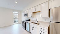 Located at 220 Quimby St NE in Grand Rapids, Michigan, this efficiently designed studio unit offers a thoughtfully arranged single-floor layout that maximizes every square foot. The open-concept living and kitchen area is anchored by a sleek galley-style kitchen outfitted with white shaker cabinetry featuring matte black hardware, light quartz countertops, a subway tile backsplash, and a full suite of stainless steel appliances including an electric range, over-the-range microwave, dishwasher, and refrigerator. Light wood-tone flooring runs throughout the space, complementing the bright, neutral color palette and recessed lighting overhead. A large window at the end of the living area invites natural light and provides outdoor views, enhancing the sense of openness. The bathroom is finished with a white vanity, matching matte black fixtures, and light wood flooring consistent with the rest of the unit. A dedicated laundry area houses a stacked washer and dryer unit, adding everyday convenience. A stylish barn-style sliding door adds a distinctive architectural detail to the interior. The overall ambiance is clean, contemporary, and well-appointed, making efficient use of the available space.