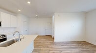 This two-floor space is designed with a clean, contemporary aesthetic defined by crisp white walls, light wood-look flooring, and an abundance of recessed lighting throughout. The open-concept main living area flows seamlessly from the kitchen, creating a bright and versatile space ideal for both everyday living and entertaining.

The kitchen is a standout feature, anchored by a large center island with a white quartz countertop and an integrated sink. White shaker-style cabinetry extends to the ceiling, maximizing storage, while stainless steel appliances—including a gas range, microwave, and French door refrigerator—complete the modern setup.

The living area is open and spacious, illuminated by recessed lighting and a smart thermostat mounted on the wall. Multiple bedrooms are found throughout the space, each featuring natural light from sizable windows fitted with blinds. Flooring varies by room, with light wood-look planks in some areas and plush carpet in others.

Bathrooms include a tub-shower combination with chrome fixtures and a dedicated walk-in shower finished in marble-look tile with sliding glass doors—adding a refined touch to the overall design.