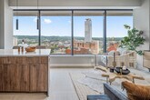 This well-appointed 1-bedroom, 1-bathroom residence offers a thoughtfully designed layout across a single floor. The open-concept kitchen and living area serves as the heart of the home, where warm wood-grain cabinetry, a white quartz peninsula with bar seating, and stainless steel appliances create a sleek, functional kitchen. Slim pendant lights hang above, adding a contemporary touch. Light-toned herringbone-pattern flooring flows throughout, enhancing the sense of space and continuity. The living area is anchored by floor-to-ceiling windows that frame expansive city views, flooding the space with natural light. A welcoming hallway with a sliding barn door connects the main living areas to the private quarters. The bedroom is a calm retreat, featuring a spacious closet, light neutral walls, and ample room for a full furniture arrangement. The bathroom is clean and modern, showcasing a glass-enclosed walk-in shower, wood-toned vanity, and elegant tiled flooring in a herringbone pattern that mirrors the rest of the home. Every detail of this residence reflects a cohesive modern aesthetic with warm, natural accents throughout.