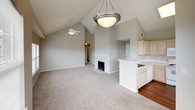 This single-floor residence offers a thoughtfully designed layout that balances functionality and comfort throughout. The kitchen is equipped with light maple cabinetry extending to the ceiling for ample storage, white appliances including a range, microwave, and refrigerator, and durable hardwood-style flooring that adds warmth to the space. Light-toned countertops and a stainless steel sink complete the practical kitchen setup. The living and dining areas are generously sized, featuring plush neutral carpeting and multiple large windows fitted with blinds that invite abundant natural light while providing privacy. A ceiling fan adds both comfort and a finishing touch to the main living space. The bedrooms are carpeted and well-proportioned, each featuring ceiling fans with lighting and ample closet space. One bedroom includes a walk-in closet outfitted with wire shelving and hanging rods, offering excellent organization potential, while another features a standard reach-in closet with bifold doors. The primary bedroom connects to a full bathroom finished with hardwood-style flooring, a tub-shower combination with white tile surround, a vanity with a wide mirror, light wood cabinetry, and chrome fixtures. The neutral, warm-toned color palette throughout creates a cohesive and inviting atmosphere across the entire floor plan.