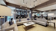 This elegant single-floor amenity space is designed with a modern, upscale aesthetic that seamlessly blends comfort and functionality across several distinct zones. The main lounge area is anchored by a pair of plush, neutral-toned sofas accented with navy throw pillows, arranged around a sleek marble coffee table. A dramatic floor-to-ceiling bookcase with diagonal shelving—illuminated by accent lighting and styled with books and decorative objects—serves as a striking focal point, with an embedded flat-screen television at its center. Pendant lighting and wall sconces provide warm, layered illumination throughout. Large floor-to-ceiling windows flood the lounge with natural light and offer views of the lush outdoor greenery beyond. Adjacent to the lounge, a casual dining and social area features high-top tables and bar-height seating alongside a beverage station, creating an inviting space for informal gatherings. A dedicated games room houses a full-size billiards table set beneath pendant lights, with a wall-mounted television and cue rack completing the entertainment setup. A quieter alcove offers round-table seating in a more intimate setting, ideal for small meetings or relaxed conversation. Large-format porcelain tile flooring and warm wood-toned wall paneling unify the space with a refined, cohesive character throughout.