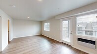 Located at 4719 W Garden Springs Rd in Spokane, WA, this single-floor unit offers a clean, modern layout designed to maximize every square foot. The living room is bright and welcoming, finished with light-toned laminate hardwood flooring that runs throughout the space. Multiple windows fitted with blinds allow natural light to fill the room, while a glass-panel exterior door provides direct outdoor access and additional brightness. Neutral beige walls and white trim create a fresh, cohesive aesthetic throughout.

The combined dining and kitchen area is a functional highlight of the unit. The kitchen features rich, warm-toned cabinetry with sleek hardware, light granite-style countertops, a stainless steel sink, and black appliances including a range, over-the-range microwave, and refrigerator. A pendant light fixture accents the dining area, adding character to the open layout.

A dedicated laundry area with a full-size washer and dryer adds significant everyday convenience. The bathroom completes the layout with clean, understated finishes consistent with the rest of the unit. Throughout the space, recessed lighting and wall-unit climate control round out the practical, well-appointed design of this Spokane residence.
