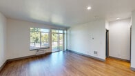 Located in Liberty Lake, WA, this well-appointed 1-bedroom, 1-bathroom unit offers a thoughtfully designed layout across a single floor. The open-concept living room and kitchen area is anchored by warm wood-style flooring and large windows that flood the space with natural light, offering pleasant views of the surrounding greenery. A sliding glass door leads to a private balcony, extending the living space outdoors. The kitchen is outfitted with gray shaker-style cabinetry, a white subway tile backsplash, stainless steel appliances including a refrigerator and electric range, and a light countertop with a peninsula that separates it from the living area. A dedicated hallway off the kitchen provides access to a stacked in-unit washer and dryer, adding everyday convenience. The bedroom features plush carpeting, a wide window with blinds overlooking mature trees, and a baseboard heating unit. A closet provides dedicated storage. The bathroom includes a gray vanity with white countertop, a large mirror, and a shower-tub combination. Throughout the unit, clean white walls, recessed lighting, and a neutral palette create a bright, modern, and move-in ready atmosphere.
