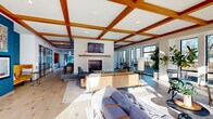 Located at 730 1/2 N First St in Minneapolis's vibrant North Loop neighborhood, this generously sized single-floor space offers an impressive open-plan layout that seamlessly blends living and dining areas. The interior is immediately defined by its signature coffered ceiling with rich warm-toned wood beams, creating a striking architectural focal point that spans the length of the space. Wide-plank light hardwood flooring runs throughout, lending a clean, contemporary aesthetic underfoot.

The living area centers around a sleek, tile-surround fireplace with a natural wood mantle, providing a welcoming anchor for multiple seating arrangements. Floor-to-ceiling windows line the perimeter walls, flooding the interior with natural light while offering open views of the surrounding greenery and outdoor patio areas. Sliding glass doors connect directly to an exterior courtyard, extending the sense of space and enabling seamless indoor-outdoor flow.

The dining zone accommodates generous group seating, complemented by a kitchen island ideal for casual gatherings. A dedicated lounge nook features bistro-height tables positioned directly in front of large picture windows, perfect for individual work or informal meetings. Bold accent walls in deep teal add visual depth and modern character, while carefully curated artwork enhances the contemporary ambiance throughout this thoughtfully designed communal space.