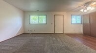 This 560-square-foot, single-floor apartment at 800 N Smith Rd, Apt X32 in Bloomington, Indiana offers a practical and functional layout across two bedrooms and one closet. The unit features wall-to-wall carpet throughout, complemented by warm wood-toned baseboards and trim that provide a consistent aesthetic across all rooms. The main living area is bright and open, benefiting from multiple windows with blinds that allow ample natural light and views of surrounding greenery. A dedicated entry door connects directly to this space. The primary bedroom measures a generous 320 square feet, offering substantial room for furnishings, and includes a window for natural light and ventilation. The second bedroom is comparably well-sized, also carpeted, with a ceiling light fixture and a window. A hallway connects the rooms, featuring hardwood-style flooring and access to a closet, adding to the unit's storage capacity. The kitchen area is visible from the main space and includes cabinetry and hardwood-style flooring. Throughout the unit, white walls provide a clean, neutral backdrop. The overall ambiance is straightforward and functional, well-suited for everyday living in a residential Bloomington neighborhood.