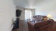 Located at 460 Sivley Rd in Hopkinsville, Kentucky, this single-floor residence offers a well-organized layout with a variety of functional living spaces. The living room serves as the heart of the home, featuring plush carpeting, a textured ceiling, and a sliding glass door with vertical blinds that opens to a private balcony, allowing ample natural light to fill the space. Adjacent to the living area is a dedicated dining space, comfortably sized for a full dining set, and positioned conveniently next to the kitchen. The galley-style kitchen is efficiently designed with white cabinetry, generous counter space, a double sink, and hardwood-style flooring, providing a practical and clean workspace. The residence includes two bedrooms, each carpeted and filled with natural light from windows with blinds. The primary bedroom offers room for a full bedroom suite with a desk area, while the secondary bedroom features a built-in closet and direct access to a bathroom. The bathroom is appointed with hardwood-style flooring, a wide vanity with a single sink, and clean white fixtures. Throughout the space, the neutral color palette and practical layout create a comfortable and functional living environment.
