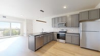 Located at 419 Third St N in Fargo, North Dakota, this well-designed one-bedroom, one-bathroom unit offers a thoughtfully arranged floor plan that maximizes every square foot. Light hardwood flooring flows throughout the main living areas, creating a warm, cohesive aesthetic accented by crisp white walls and clean modern finishes.

The open-concept kitchen and living area serves as the heart of the unit. The kitchen is equipped with gray shaker-style cabinetry, a full suite of stainless steel appliances including a range, microwave, dishwasher, and refrigerator, along with a dark-topped peninsula that doubles as additional workspace and a natural divider between the kitchen and living space. A wood-accented pendant light adds a contemporary touch overhead.

The living area opens to a private balcony through a large sliding glass door, offering abundant natural light and pleasant outdoor views of the surrounding landscape. The bedroom is a comfortable, well-proportioned room featuring plush carpeting, a large window overlooking the balcony, and a closet, creating a calm and restful retreat.

The bathroom features a clean, all-white walk-in shower surround. A dedicated laundry room with a full-size Whirlpool front-loading washer and dryer and overhead wire shelving adds exceptional everyday convenience to this modern Fargo residence.