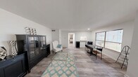 This thoughtfully designed one-bedroom, one-bathroom residence offers a clean, minimalist aesthetic throughout its single-floor layout. Light wood-style flooring flows seamlessly from room to room, complemented by crisp white walls that maximize the sense of brightness and openness.

The living room serves as the heart of the unit, offering a well-proportioned gathering space with enough room to accommodate comfortable seating arrangements. The neutral tones and light-filled atmosphere create a calm, welcoming ambiance ideal for both relaxing and entertaining.

The bedroom is a comfortable retreat, featuring a window that invites natural light and outdoor views, built-in shelving that adds practical storage, and ample space for a full sleeping arrangement with accompanying furniture. The room's simple, clean design ensures versatility for personalization.

The bathroom is finished in a classic all-white palette, featuring a tiled tub-shower combination with floor-to-ceiling square white tiles, a white vanity with brushed nickel fixtures, and a mirrored medicine cabinet — combining functionality with a timeless, clean aesthetic.

The kitchen connects efficiently to the living and dining areas, rounding out a cohesive and practical floor plan. Throughout the space, the consistent use of light tones, wood-style flooring, and clean finishes creates a unified, move-in-ready environment.