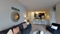 Located at 1 Mirada Dr N in Lewis Center, Ohio, this single-floor residence offers a thoughtfully designed open-concept layout that seamlessly connects the living and kitchen areas. The living room is warm and inviting, featuring neutral-toned walls, plush carpeting, and decorative touches such as a striking round mirror that adds depth and character to the space. Large, comfortable seating anchors the room, creating an ideal setting for relaxation or entertaining.

The kitchen is a standout feature, showcasing dark espresso cabinetry paired with light stone countertops for a bold contrast. Stainless steel appliances, including a refrigerator and microwave, provide a sleek, modern aesthetic. A breakfast bar with bar-height seating offers a casual dining option and reinforces the open flow between the kitchen and living spaces. Pendant lighting above the bar adds a refined touch, complementing the track lighting that illuminates the cabinetry and workspace below.

The transition between the carpeted living area and the hard-surface flooring of the kitchen is clean and well-defined, contributing to the overall cohesive design. The neutral color palette throughout the space creates a bright, airy ambiance, making the interior feel open and welcoming. This residence combines functional layout with modern finishes to deliver a comfortable and stylish living environment.