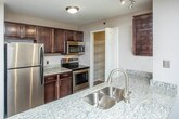 Located at 15900 Silver Pkwy in Fenton, Michigan, this single-floor unit offers a clean, modern aesthetic throughout its well-organized layout. The open living area features a seamless transition between plank-style flooring and plush carpeting, creating distinct zones while maintaining a cohesive flow. Large windows allow natural light to fill the space, contributing to a bright and airy atmosphere.

The galley-style kitchen is thoughtfully appointed with rich dark cabinetry, granite countertops, a stainless steel sink, and a full suite of stainless steel appliances including a refrigerator, microwave, and range. Wood-look flooring runs through the kitchen, adding warmth and easy maintenance.

The bedrooms are generously sized, each finished with soft neutral carpet and windows fitted with slatted blinds that offer both light control and outdoor views. The primary bedroom includes a walk-in closet area that connects directly to a private en-suite bathroom.

Two full bathrooms serve the unit, each featuring a tub-shower combination with a curved rod, wood-look tile flooring, and dark vanity cabinetry topped with granite counters. A dedicated laundry area with washer and dryer hookups adds practical convenience. Neutral gray wall tones throughout the unit create a versatile, move-in-ready environment.