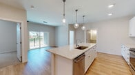 This well-appointed single-floor residence showcases a thoughtfully designed open-concept layout that seamlessly connects the kitchen, dining, and living areas. The kitchen is a standout feature, centered around a large island with light stone countertops, an undermount sink, and a stainless steel dishwasher. A trio of elegant glass pendant lights hang above the island, complementing the recessed ceiling lights throughout. White shaker-style cabinetry extends to the ceiling, paired with a subway tile backsplash and a full suite of stainless steel appliances, including a range, over-the-range microwave, and a French door refrigerator. Warm-toned hardwood flooring flows throughout the main living areas, creating a bright and cohesive aesthetic. The living area opens directly to a private balcony through sliding glass doors, inviting natural light and outdoor views. Bedrooms are carpeted for comfort and feature closets and windows overlooking greenery. The unit includes two full bathrooms finished in neutral tones with white cabinetry, tile flooring, and tub-shower combinations. A dedicated laundry closet houses a stacked full-size washer and dryer alongside wire shelving for added storage. The overall design is clean, modern, and move-in ready.