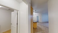 This single-floor residence offers a thoughtfully designed open layout that connects the kitchen, dining, and living areas seamlessly. The kitchen serves as a central highlight, featuring light maple cabinetry, striking dark granite countertops, and a full suite of stainless steel appliances including a gas range, microwave, dishwasher, and a French door refrigerator with an ice and water dispenser. A curved central island with pendant lighting above adds both workspace and visual appeal, while tile flooring grounds the space with a clean, practical finish. The open living and dining area transitions from tile to plush carpet, creating a warm and comfortable atmosphere. A ceiling fan and a chandelier provide layered lighting options, while a window allows natural light to brighten the room. A hallway connects to additional rooms, including a bathroom outfitted with light maple vanity cabinetry, a dark granite countertop, a large mirror, and tile flooring. Throughout the space, white walls and crisp trim provide a neutral, versatile backdrop, while interior doors with louvered panels and paneled white bi-fold doors add classic architectural details. The overall layout is practical and inviting, offering a cohesive aesthetic throughout.