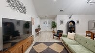 Located at 125 Parker Pl in LaGrange, GA, this single-floor space offers a well-designed open-concept layout that combines a kitchen and living room into one cohesive, functional area. Vaulted ceilings elevate the interior throughout, creating an airy, expansive feel that belies the compact footprint.

The kitchen is outfitted with soft gray shaker-style cabinetry, white quartz countertops, and a white herringbone tile backsplash that adds texture and visual interest. Stainless steel appliances — including a full-size French door refrigerator, dishwasher, and microwave — provide modern functionality. Open floating shelves display decorative greenery and accents, contributing to the space's curated aesthetic.

The living area is bright and welcoming, anchored by light wood-look flooring that runs seamlessly throughout. French doors at the far end of the room invite natural light and provide access to the exterior. The vaulted ceiling continues here, amplifying the sense of openness. A built-in arched niche adds an architectural detail that complements the mid-century modern furnishing style evident throughout the space.

Together, the kitchen and living room form a cohesive, well-appointed interior that balances modern design with warm, inviting character — ideal for both relaxing and entertaining.