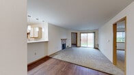 This single-floor, 2-bedroom, 2-bathroom home offers a practical and comfortable layout across a modest yet efficiently utilized footprint. The combined kitchen and living area serves as the heart of the home, where hardwood flooring in the kitchen transitions seamlessly to plush carpeting in the living room. The kitchen features light wood cabinetry, a breakfast bar peninsula, and stylish pendant lighting overhead, with a ceiling fan adding to the functionality of the space. A brick fireplace anchors the living room, adding warmth and character, while a sliding glass door fills the space with natural light and provides direct access to the outdoors, offering views of a green lawn and surrounding trees.

The primary bedroom is generously sized, carpeted, and includes ample closet space, while the second bedroom features carpet flooring and a window that brings in natural light. Two closets throughout the home offer practical storage. The two bathrooms include one with a tub/shower combination with tile flooring and another with a walk-in shower unit. A dedicated utility room provides additional functionality. The attached garage, accessible from the interior, features an automatic door and concrete flooring, completing this well-rounded and move-in-ready home.