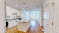 Located at 900 SE Third Ave in Ocala, FL, this single-story, 4-bedroom, 2-bathroom home offers a clean, modern aesthetic with thoughtful finishes throughout. The open-concept kitchen and living area serves as the heart of the home, featuring warm hardwood-style flooring, white shaker cabinetry, granite countertops, a large center island with pendant lighting, and a full suite of stainless steel appliances including a refrigerator, range, and microwave. The kitchen flows seamlessly into the living area, which is brightened by natural light from large windows and finished with a ceiling fan overhead. A glass door provides additional access and light to the living space. The four bedrooms offer a comfortable and versatile layout, with the primary bedroom featuring hardwood-style flooring and ample natural light, while the additional bedrooms are carpeted and each include windows with views of the surrounding neighborhood. Three closets provide generous storage throughout. Both bathrooms are finished consistently with granite-topped white vanities, large mirrors, and hardwood-style flooring. One bathroom includes a tub/shower combination. The overall design presents a bright, neutral palette that creates a welcoming and functional living environment.