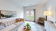 Located at 5945 Arlo Way in Indianapolis, IN, this well-designed one-bedroom, one-bathroom home offers a clean, modern aesthetic throughout its single-floor layout. Light wood-style flooring flows through the main living areas, complemented by crisp white walls and recessed lighting that create a bright, airy atmosphere.

The living room is a welcoming focal point, featuring French doors that open to a lush green outdoor view, allowing natural light to fill the space. A dedicated area for a sideboard and artwork adds a refined, curated touch to the room's character.

The kitchen is thoughtfully appointed with white shaker cabinetry, light quartz countertops, a peninsula with a sink, and a full suite of stainless steel appliances including a refrigerator, electric range, and microwave. Recessed lighting enhances the clean, functional design.

The spacious bedroom features plush carpeting, a large window overlooking a green outdoor setting, and ample wall space for artwork. An adjacent closet provides generous storage. The hallway features built-in double-door closets and a decorative round mirror, adding both practicality and style.

The bathroom offers a glass-enclosed walk-in shower with tile surround and built-in open shelving for organized storage. Every detail reflects a cohesive, modern design sensibility.